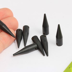 Peut inclure: Huit perles en bois de forme conique noires avec un trou en haut. Les perles mesurent environ 2,5 cm de long.