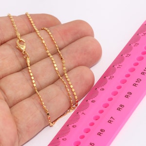 Puede incluir: Un collar de cadena de oro con un cierre de langosta. La cadena está colocada sobre una regla rosa con marcas en pulgadas.