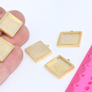 May include: Four gold-toned square pendant trays with a textured surface. The trays are approximately 1 inch in size and have a loop at the top for attaching a chain or cord.