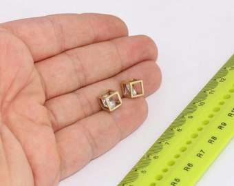 Puede incluir: Un par de pendientes de tono dorado con un diseño cuadrado. Cada pendiente presenta una piedra de circonita cúbica transparente engastada en un marco de oro.