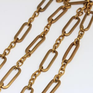Peut inclure: Gros plan d'un collier doré avec un motif répétitif de maillons rectangulaires allongés reliés par de petites chaînes. Le collier est présenté sur un fond blanc, soulignant son éclat métallique et son design.