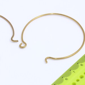 Può includere: Due cerchi in metallo dorati con un gancio ad ogni estremità. I cerchi hanno un diametro di circa 5 cm. Un righello verde è sullo sfondo.