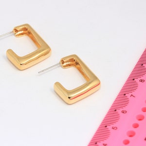 May include: A pair of gold square hoop earrings with a slightly rounded edge. The earrings are shown next to a pink ruler.