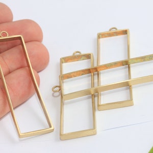 Può includere: Quattro cornici rettangolari in metallo dorato con un anello in cima per appendere. Le cornici sono di dimensioni diverse e sono impilate l'una sull'altra.