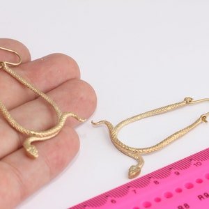 Op de afbeelding: Een paar gouden slangen oorbellen. De oorbellen zijn gemaakt van getextureerd metaal en zijn gevormd als een slang met zijn kop opgerold. De oorbellen zijn ongeveer 5 cm lang.