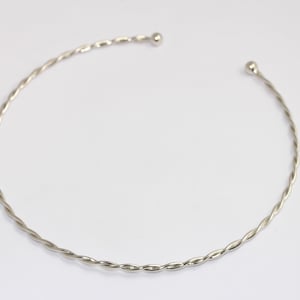 Op de afbeelding: Een zilveren armband van gedraaid draad met kleine ronde balletjes aan beide uiteinden.