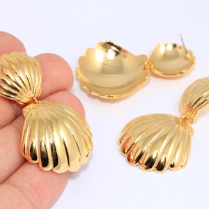 May include: A pair of gold-tone shell-shaped dangle earrings. The earrings are made of two overlapping shells, with the top shell being smaller than the bottom shell.