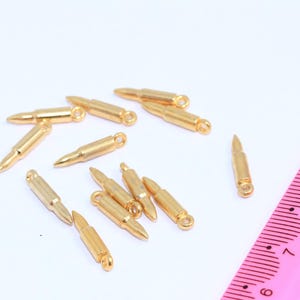 May include: A group of gold-colored bullet charms with a loop at the top for attaching to jewelry or other crafts.