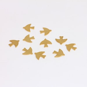 May include: A collection of ten gold-colored metal bird charms, scattered on a white surface.
