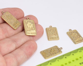 May include: Five gold-coloured metal charms shaped like tarot cards, each featuring the "The Sun" card design. The charms are on a white surface with a green ruler in the background.
