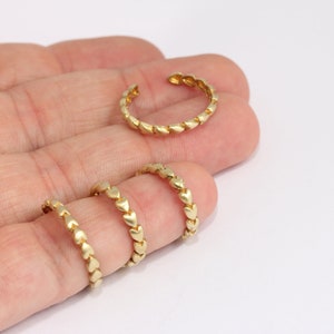 May include: Three gold rings made of linked heart shapes. The rings are different sizes and are shown on a hand.