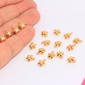 May include: A collection of 17 gold-colored star-shaped charms with a loop for attaching to jewelry or other crafts.