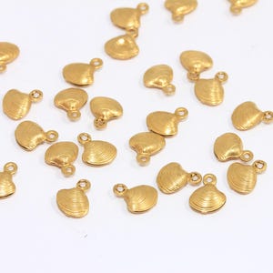 Può includere: Una collezione di ciondoli a forma di conchiglia di vongola in metallo dorato con un anello per attaccarli a gioielli o altri oggetti artigianali.