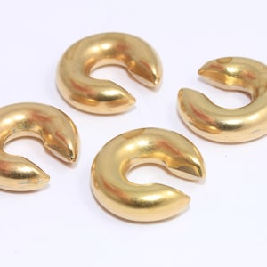 May include: Four gold-colored, crescent-shaped objects are arranged on a white surface. Each object has a smooth, rounded form with a hollow center. The objects appear to be made of metal and have a shiny finish.