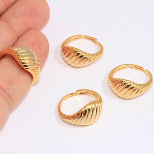May include: Three gold-toned rings with a ridged, curved design. The rings are shown on a white surface.