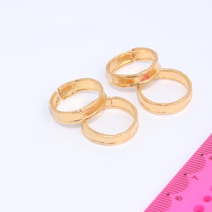 Op de afbeelding: Vier gouden ringen die op elkaar gestapeld zijn. De ringen zijn eenvoudig en hebben een gehamerde textuur. Een roze liniaal met zwarte markeringen is op de achtergrond.