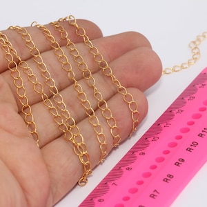 Puede incluir: Cadena dorada con eslabones en forma de corazón, mostrada en una mano junto a una regla rosa. La regla muestra medidas en centímetros. La cadena es de color oro brillante.