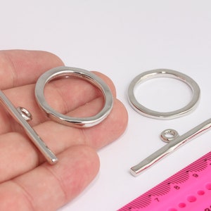 May include: Silver-toned toggle clasps, including two bars and two rings, are displayed against a white background. The clasps are shown in a hand, with a pink ruler in the background. These clasps are ideal for jewelry making.