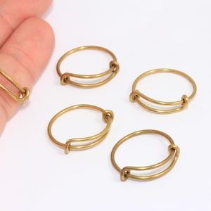 Könnte beinhalten: Fünf goldfarbene Metallringe mit einem Doppel-Loop-Design. Die Ringe sind alle gleich groß und in einem Halbkreis auf einer weißen Oberfläche angeordnet.