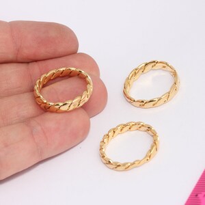 Può includere: Tre anelli dorati con un designo intrecciato. Gli anelli sono su una superficie bianca.
