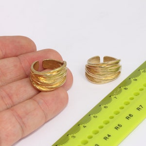 May include: Two gold-toned rings with a textured, wavy design. The rings are shown on a hand and next to a ruler.