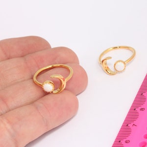 May include: Two gold rings with a crescent moon design and a white opal stone. The rings are shown on a hand and a pink ruler.