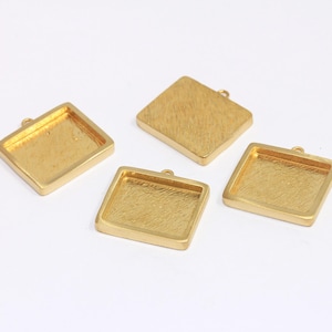 Könnte beinhalten: Vier goldfarbene quadratische Anhänger-Tabletts mit strukturierter Oberfläche. Jedes Tablett hat oben eine kleine Schlaufe zum Anbringen einer Kette oder eines Bandes. Die Tabletts sind leer und bereit zur individuellen Gestaltung.