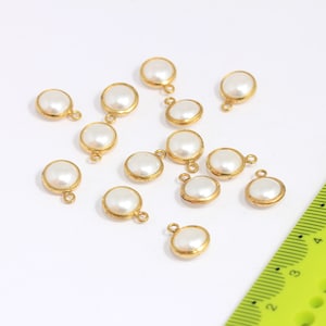 May include: A collection of 14 white pearl charms with gold-toned metal loops. The charms are scattered on a white surface.