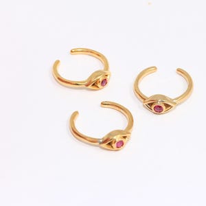 Puede incluir: Tres anillos de oro con un diseño de ojo rosa. Cada anillo tiene una pequeña piedra rosa en el centro del ojo.