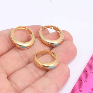 Op de afbeelding: Drie gouden ringen met een lichtblauwe steen ingelegd. De ringen zijn in verschillende maten en worden op een hand getoond.