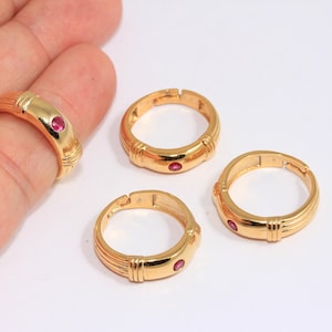 May include: Three gold rings with a single red gemstone on each. The rings are adjustable and have a simple design.