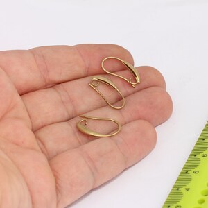 Op de afbeelding: Drie gouden oorhaken, ook wel oorbedrading genoemd, worden op een hand getoond. De haken zijn ongeveer 2,5 cm lang.