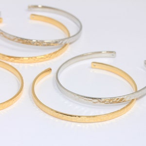 Può includere: Quattro braccialetti in metallo martellato dorati e argentati. I braccialetti sono impilati uno sopra l'altro.