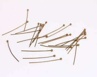 Può includere: Un mucchio di spilli con testa rotonda dorati. Gli spilli sono sparsi su una superficie bianca.