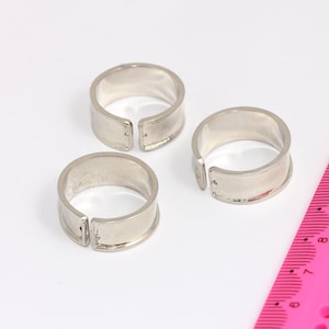 May include: Three silver metal rings with a gap in each ring. The rings are on a white surface next to a pink ruler.