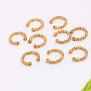 May include: Ten gold-colored twisted wire nose rings. The rings are about 1 cm in diameter.