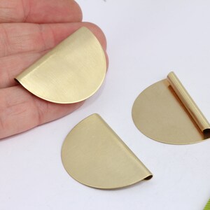 May include: Three gold-colored metal half-circle shapes. Two of the shapes are flat, and one has a rolled edge.