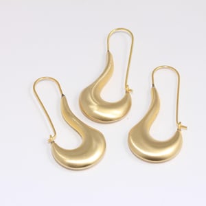 Peut inclure: Trois boucles d'oreilles dorées avec un design incurvé en forme de goutte d'eau. Chaque boucle d'oreille a un long crochet fin pour l'oreille. Les boucles d'oreilles sont présentées sur un fond blanc.