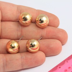 May include: Four gold-colored ball stud earrings. The earrings are shown on a hand against a white background.