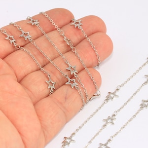 Puede incluir: Tres cadenas plateadas con dijes en forma de estrella. Las cadenas están superpuestas y se muestran en una mano.