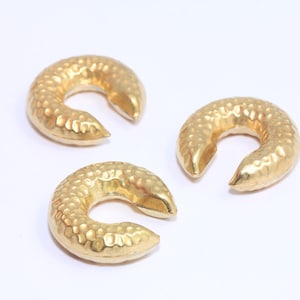 Può includere: Tre orecchini a cerchio in metallo color oro con una texture martellata. Gli orecchini hanno la forma di una mezzaluna e hanno un'apertura arrotondata.