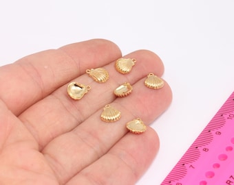 May include: A collection of small, gold-colored seashell charms. The charms vary in design, with some featuring a ribbed texture and others a smooth surface. A pink ruler is in the background.