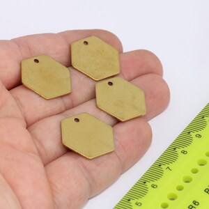 May include: Three gold-coloured hexagonal metal charms with a hole in the centre. The charms are on a hand, and a ruler is in the background.