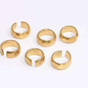 May include: Six gold-toned metal rings with a hammered texture. The rings are open on one side and are designed to be worn on the finger.