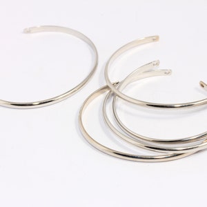 May include: Five silver bangle bracelets stacked on top of each other. The bracelets are all simple and plain, with no embellishments.