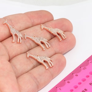 May include: Five gold-tone giraffe charms with clear rhinestones. The charms are approximately 2 inches long and are displayed on a hand.