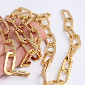 May include: A gold chain with rectangular links. The chain is lying on a hand.