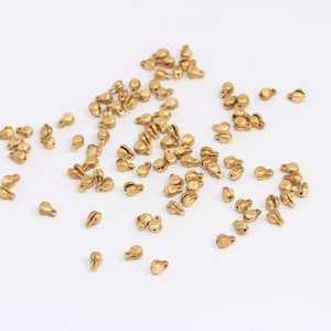 May include: A scattering of gold-toned metal beads, each with a small loop at the top. The beads are arranged in a random pattern on a white surface.