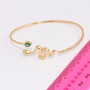 May include: A gold snake bangle bracelet with a green gemstone accent. The bracelet is open and measures approximately 6.5 inches in circumference.