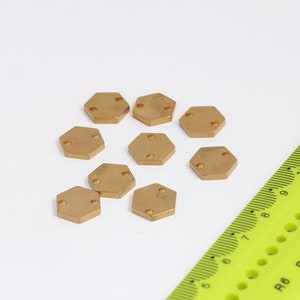 Puede incluir: Diez piezas hexagonales de metal de color dorado con pequeños puntos redondos en cada pieza. Las piezas están esparcidas sobre una superficie blanca.